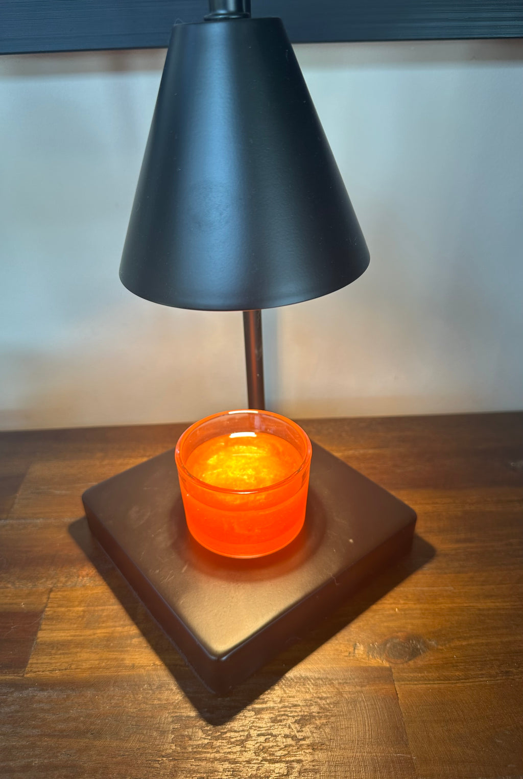 Black candle warming lamp turned on with a peach scented wickless candle sitting on base on a wood dresser
