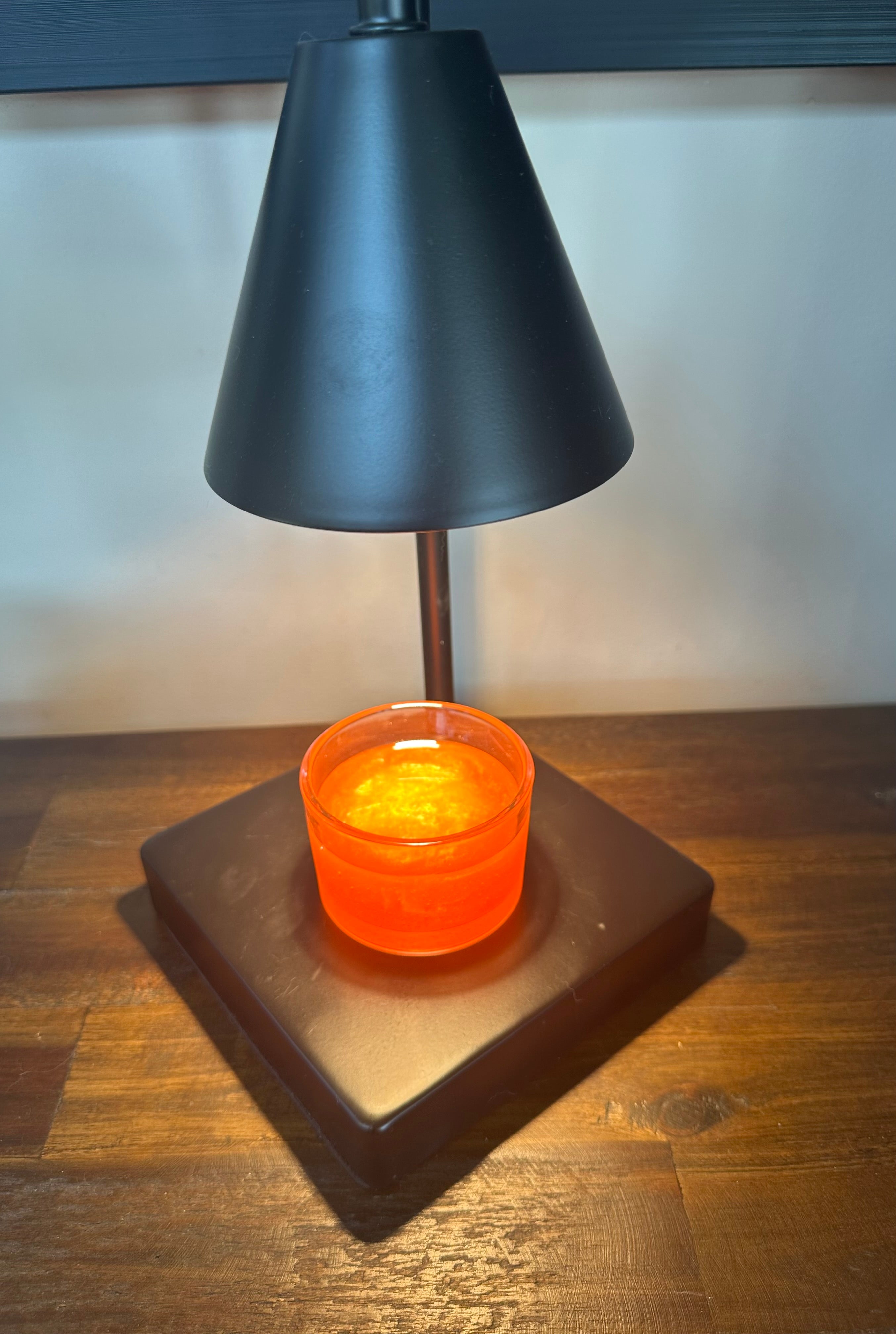 Black candle warming lamp turned on with a peach scented wickless candle sitting on base on a wood dresser