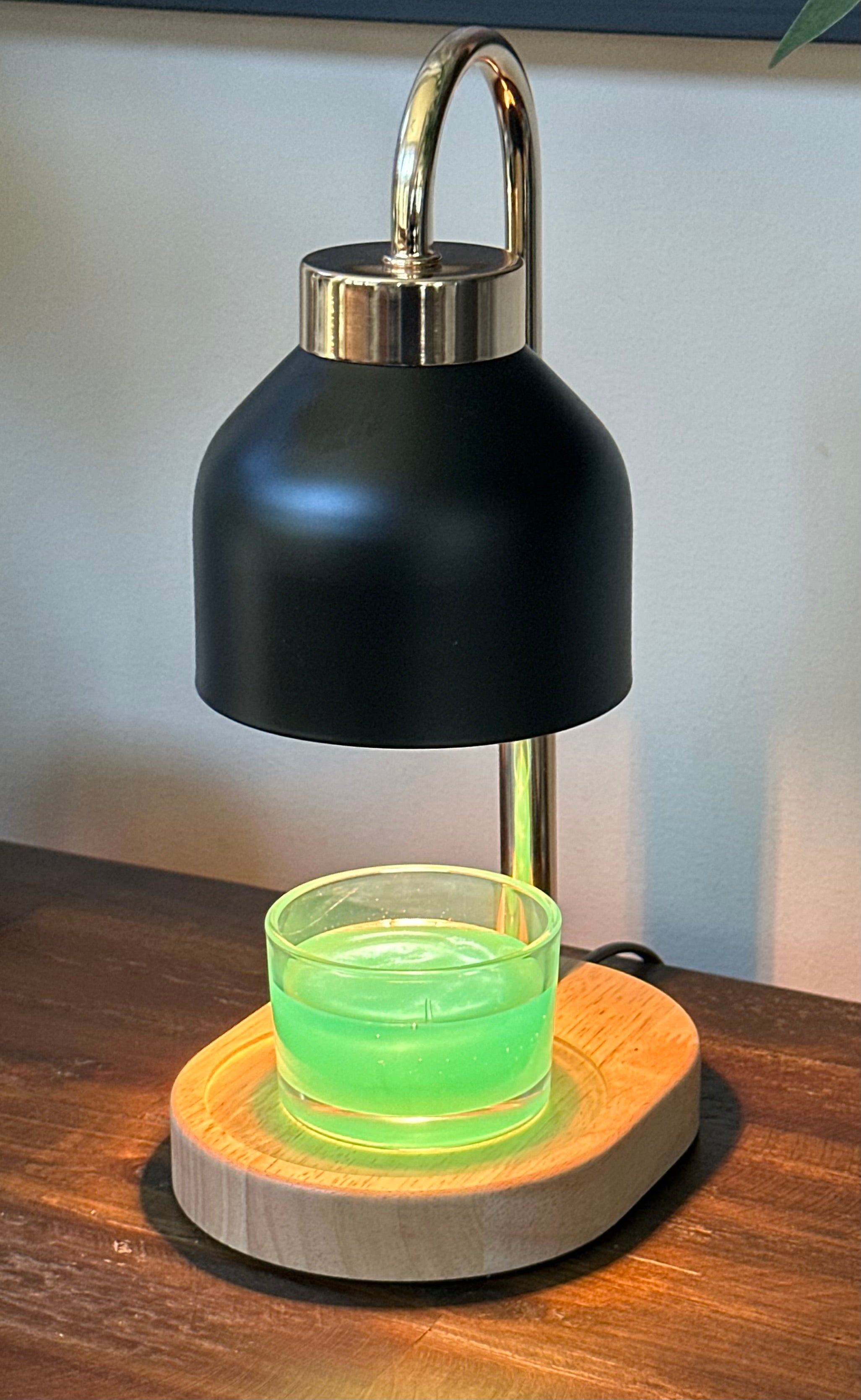 black and gold candle warming lamp turned on with a green colored Hawaiian volcano scented candle sitting on the wooden base on a wood dresser